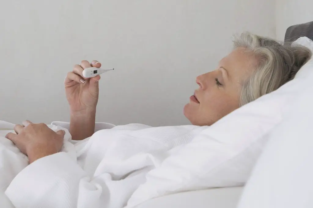 woman sick in bed with thermometer