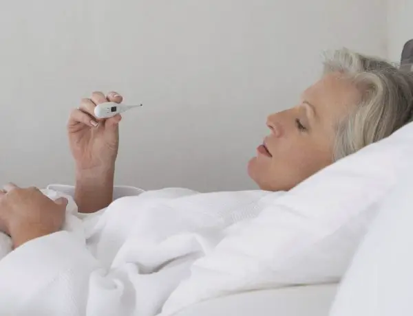 woman sick in bed with thermometer