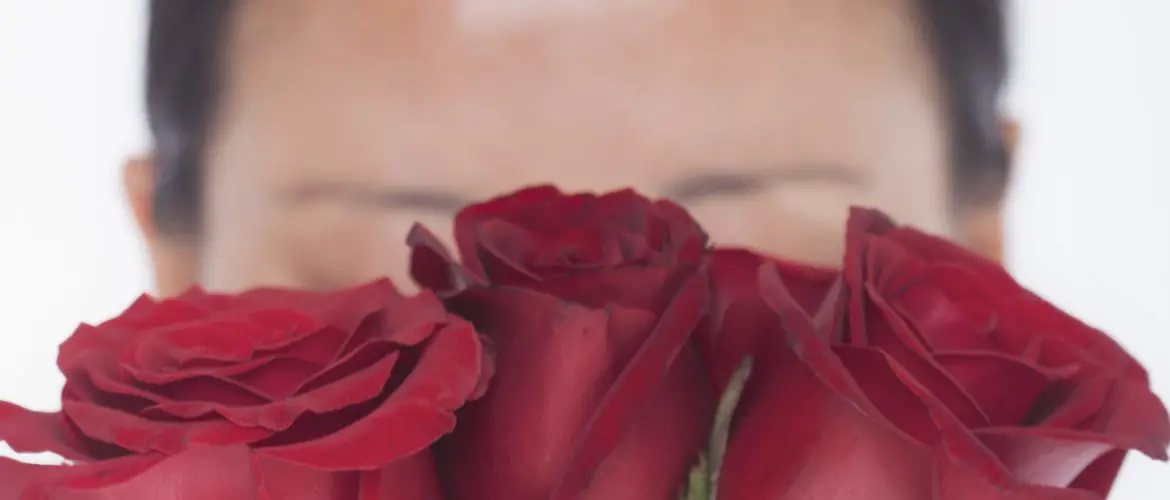 woman with rosacea hiding face behind red roses