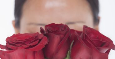 woman with rosacea hiding face behind red roses