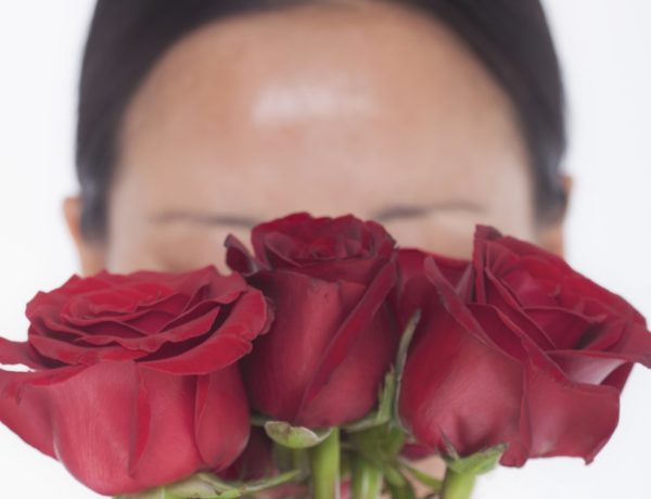 woman with rosacea hiding face behind red roses