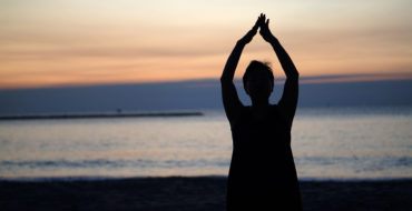Woman doing yoga on beach at sunrise