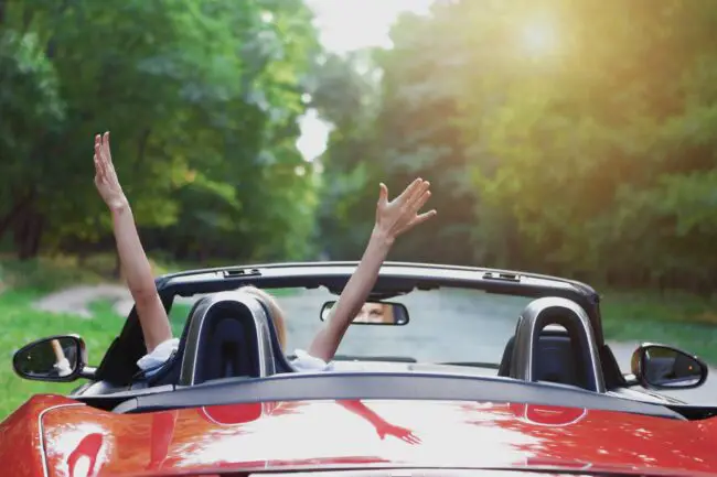 Woman waves arms in convertible