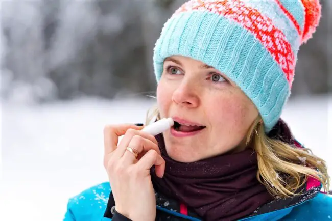 60ish woman applying lip balm in winter