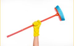 Woman wearing yellow glove holding broom over head