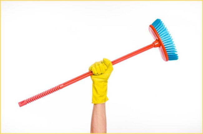 Woman wearing yellow glove holding broom over head