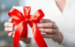 Woman in white sweater giving package with red bow