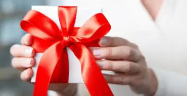 Woman in white sweater giving package with red bow