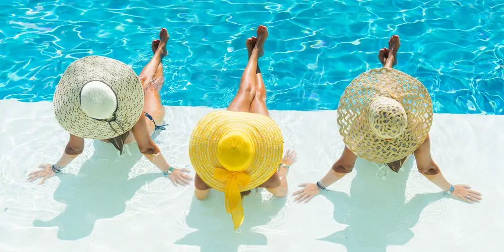 Three women wearing large straw hats in swimsuits for women over 60