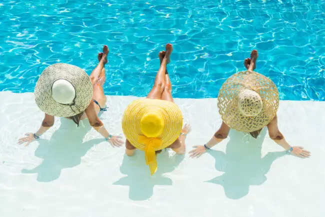 Three women wearing large straw hats in swimsuits for women over 60