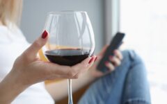 Woman holding glass of wine and tv remote control