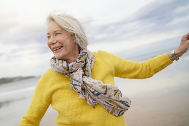 Energetic woman over 60 wearing yellow sweater on beach