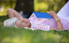Attractive woman over 60 lying on grass reading summer book